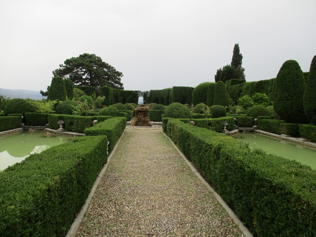 Villa Gamberaia in Florence, Italy showing a path lined with hedges and with water on either side, leading to a circular courtyard.