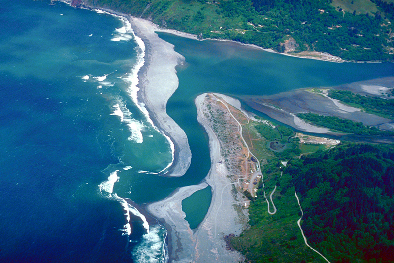 This photo shows an aerial view of the ocean on the left, and a river on the right emptying into the ocean.