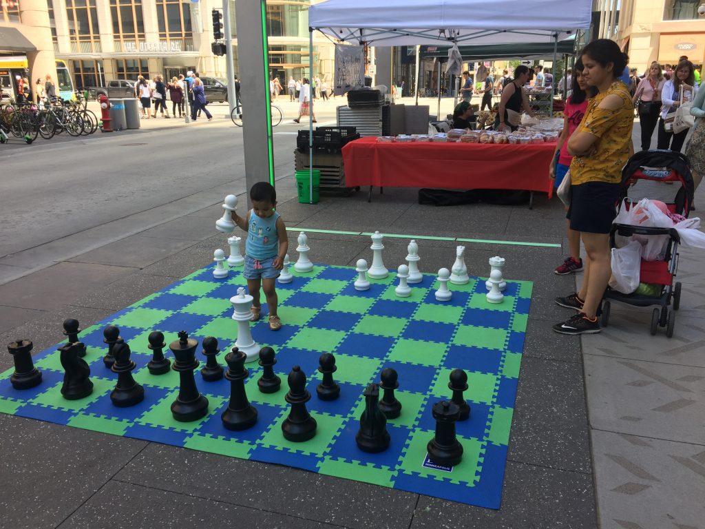 A child and adult playing on a giant chess board on Nicollet Mall.
